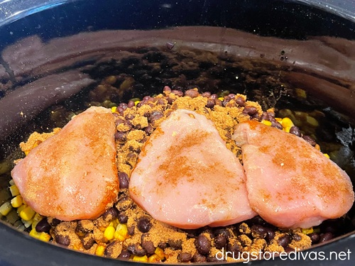 Three pieces of seasoned chicken on top of corn and beans in a slow cooker.