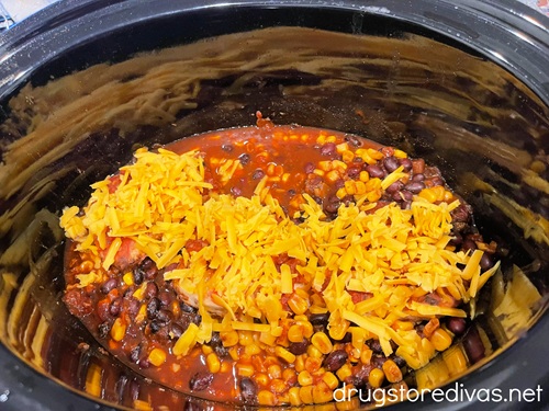Shredded cheese on top of cooked corn and beans in a slow cooker.