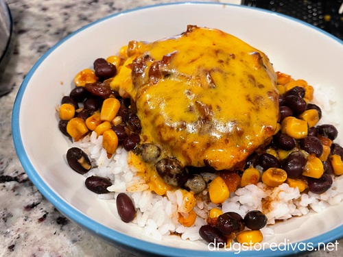 A piece of salsa chicken covered in melted cheddar cheese on top of rice, corn, and black beans in a bowl.