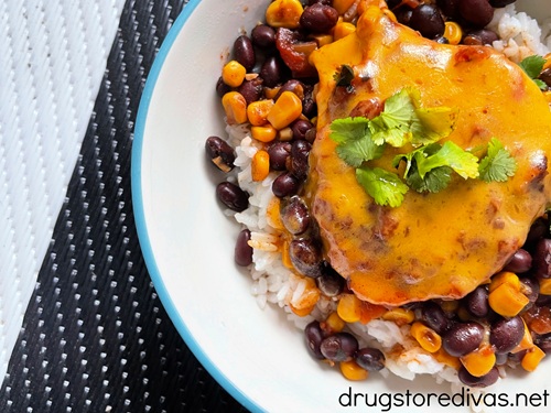 A piece of slow cooker salsa chicken, with melted cheddar cheese, on top of rice and beans and corn in a bowl.