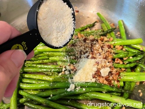 Grated parmesan cheese in a measuring cup above a pan with asparagus and chopped almonds in it.
