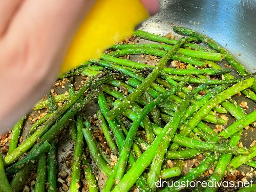 A hand holding a lemon above a pan with asparagus and chopped almonds in it.