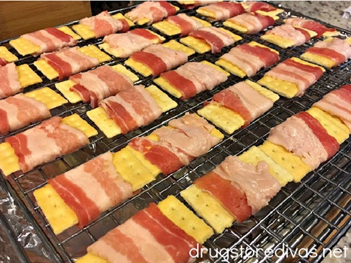 Club crackers wrapped in uncooked bacon on a wire rack.