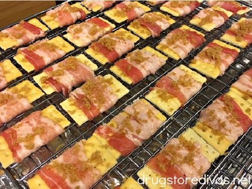 Club crackers wrapped in uncooked bacon with brown sugar on top on a wire rack.