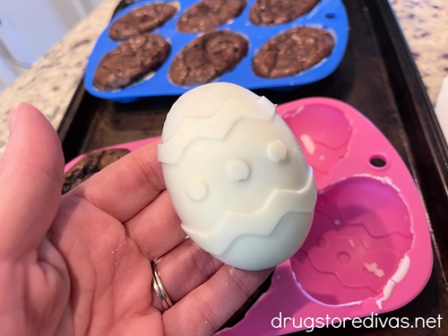 A hand holding a white chocolate covered brownie egg above a pink mold with a blue one behind it.