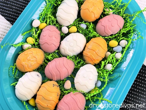 A blue oval tray with green paper shred on it, topped with yellow, pink, and white chocolate covered brownie eggs and chocolate mini eggs around them.