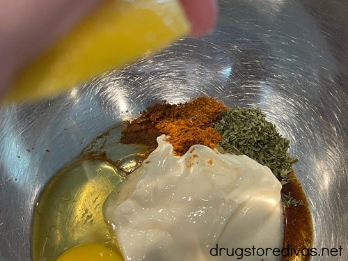 A hand squeezing half a lemon above mayo, egg, and seasoning in a metal bowl.