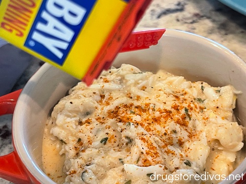 Old Bay seasoning in a container being poured on top of crab meat in a small bowl.