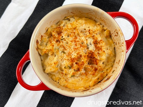 Baked crab imperial in a red mini Dutch oven on a black and white striped tablecloth.
