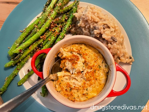 Baked crab imperial in a red mini Dutch oven on a plate with asparagus almondine and risotto.