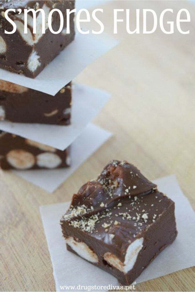 Three pieces of fudge with parchment between them stacked in the back an one with parchment in the front with the words "S'mores Fudge" digitally written on top.