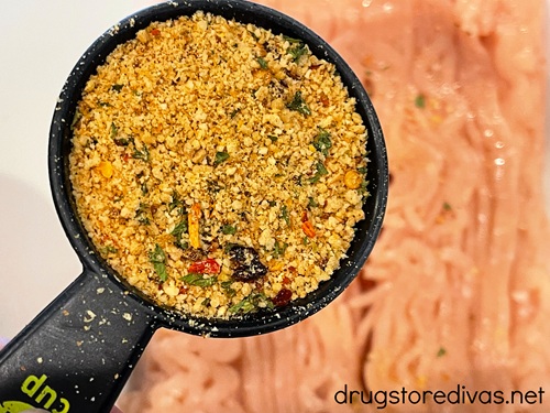 Seasoning in a measuring cup above ground chicken in a bowl.