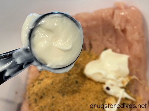 Mayo in a measuring spoon above ground chicken in a bowl.