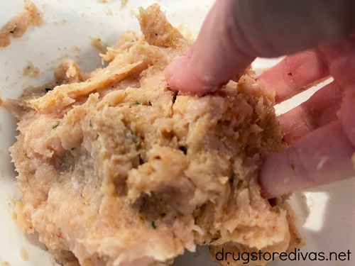 A hand mixing ground chicken.