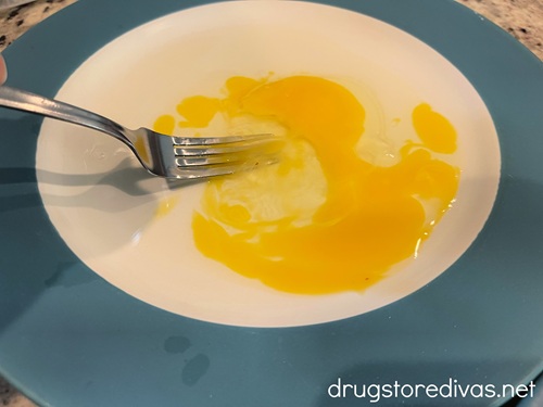 A fork scrambling an egg on a plate.