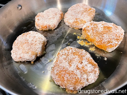 Five raw chicken patties in a silver skillet.