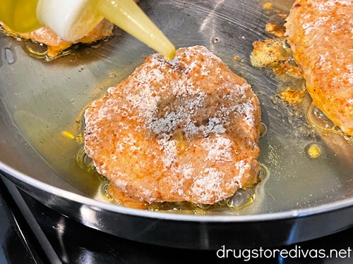 Olive oil being drizzled on a chicken patty in a skillet.