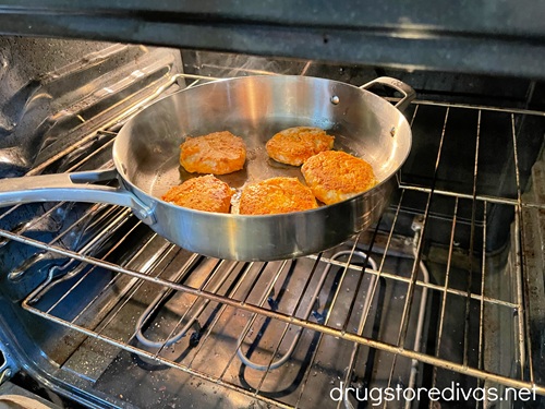 A silver skillet with five chicken patties on it in the oven.