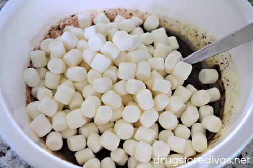 Mini marshmallows on top of melted chocolate in a white bowl with a spoon in it.