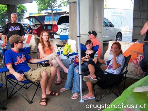 A young man and three young women under a pop up tent, tailgating before a baseball game.