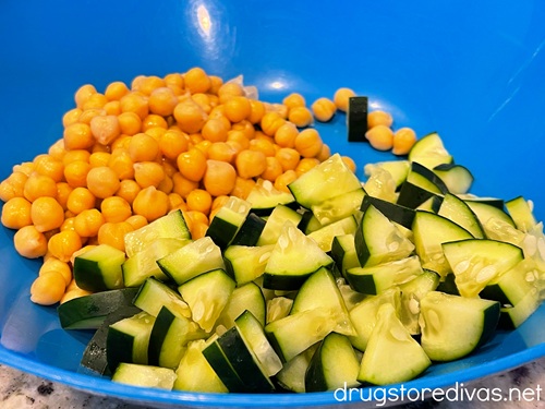Cut cucumbers and chickpeas in a blue bowl.
