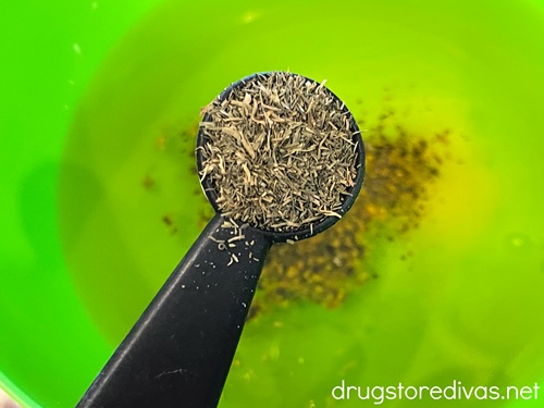 Italian seasoning in a measuring spoon over a green bowl with oil and seasoning in it.