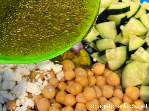 Dressing in a green bowl being poured over a bowl with cucumber and chickpeas in it.
