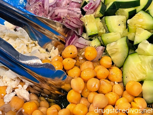 Cucumber and chickpea salad being tossed with a tongs.