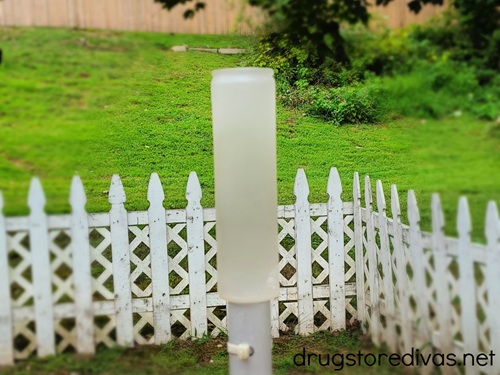 A tall candle resting in a backyard with a white fence in the background.