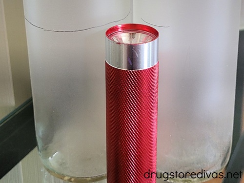A red flashlight in front of two tall candles with a pencil mark on them.