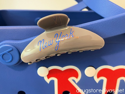 A gray claw clip that says New York on it attached to the handle of a New York Mets Bogg Bag.