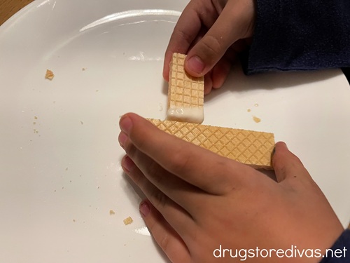 A child's hand attaching two pieces of wafer cookies together to look like a cross.