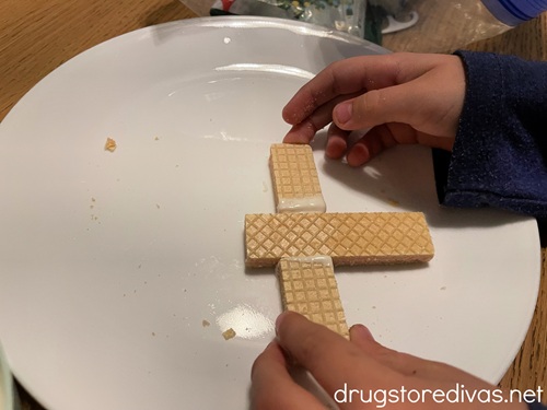 A child's hand attaching three pieces of wafer cookies together to look like a cross.