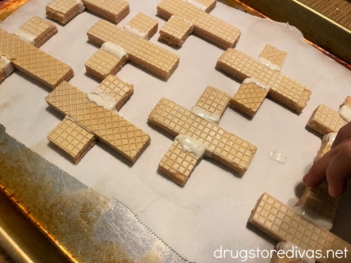 A bunch of wafer cookies shaped like crosses on a parchment paper-lined baking sheet.