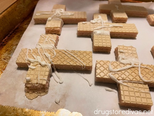 A bunch of wafer cookies shaped like crosses with white chocolate on top on a parchment paper-lined baking sheet.