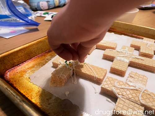 A child's hand putting sprinkles on top of wafer cookies shaped like crosses.