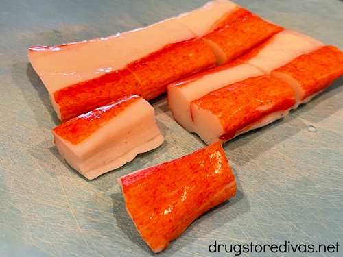 Imitation crab sticks on a blue cutting board cut into thirds.