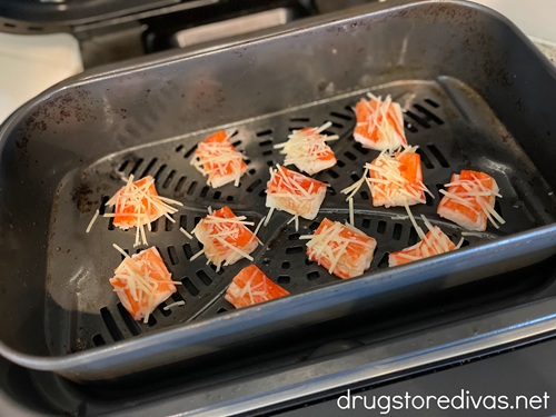 Uncooked imitation crab bites with parmesan cheese on them in an air fryer.