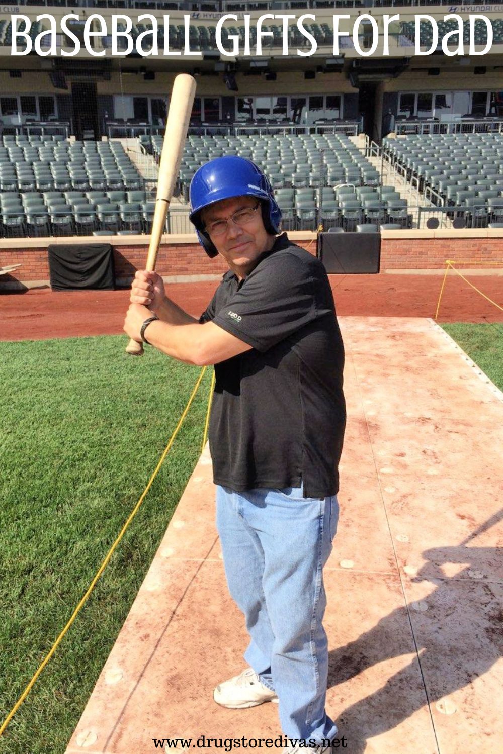 A man in a black t-shirt, jeans, and a baseball helmet holding a baseball bat like a better in a baseball stadium with the words 