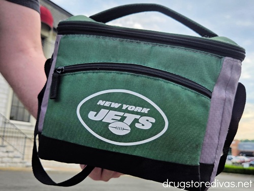 A man's hand holding a green insulated cooler with the New York Jets logo on it.