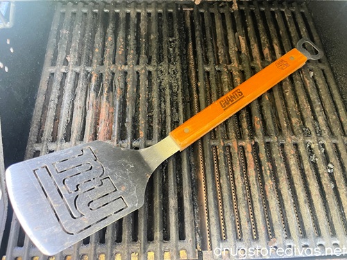 A spatula with a New York Giants logo on the blade and a bottle opener on the other end on top of grill grates.