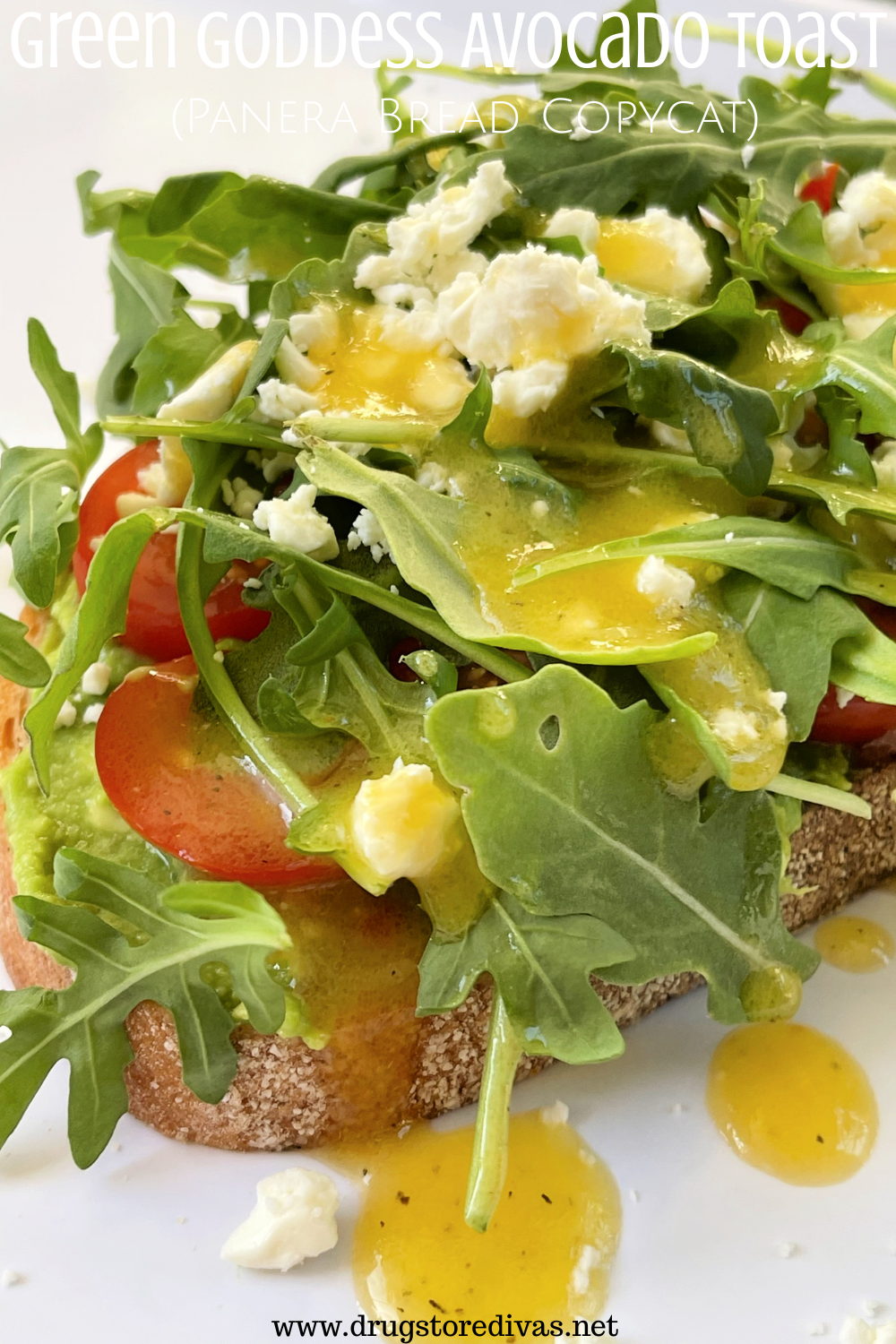 A piece of avocado toast with tomato, arugula, feta, and dressing on top and the words 