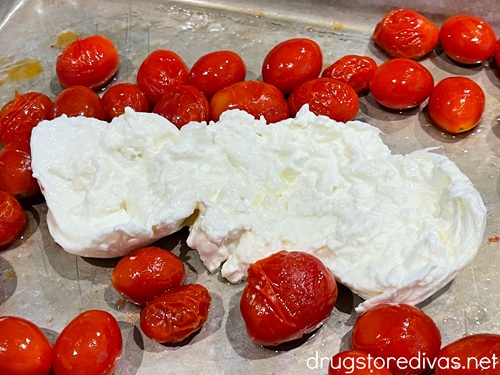 Cherry tomatoes and an open ball of burrata cheese on a silver baking sheet.