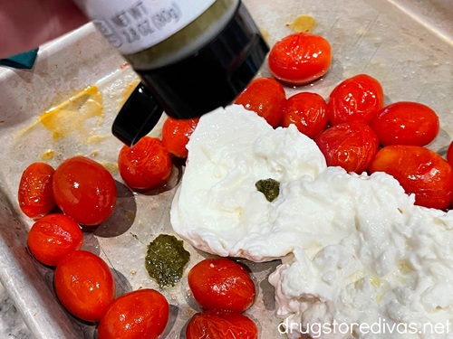 Basil paste being squeezed onto cherry tomatoes and burrata cheese on a silver baking sheet.