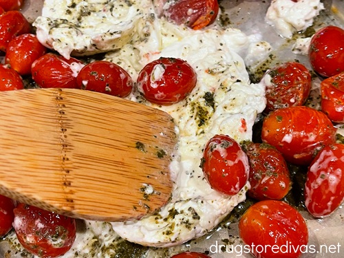 A bamboo spoon stirring cherry tomatoes, burrata cheese, and basil paste.