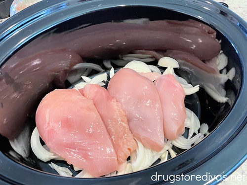 Raw chicken on top of sliced onion in a slow cooker.