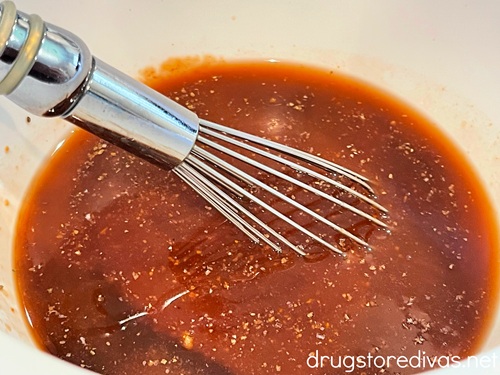 A whisk in barbecue sauce that's in a white bowl.