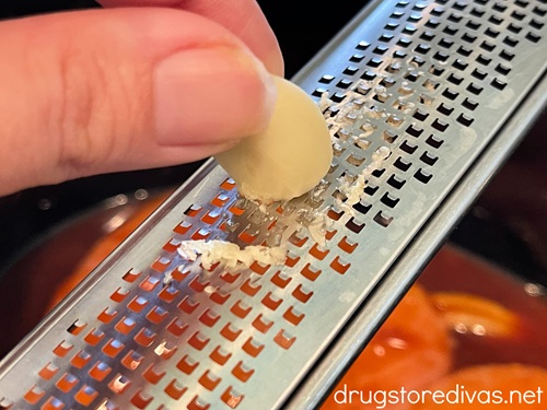 A hand grating garlic into a slow cooker.