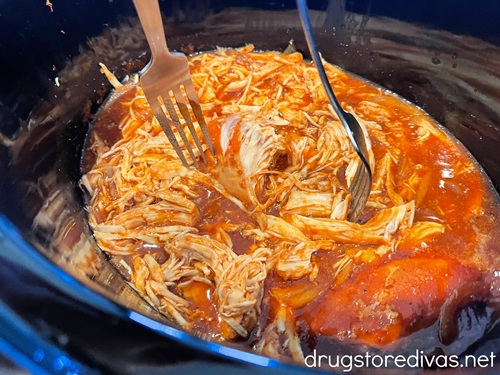 Two forks shredding barbecue chicken in a slow cooker.
