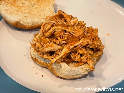 Barbecue pulled chicken on the bottom half of a hamburger bun with the top nearby.